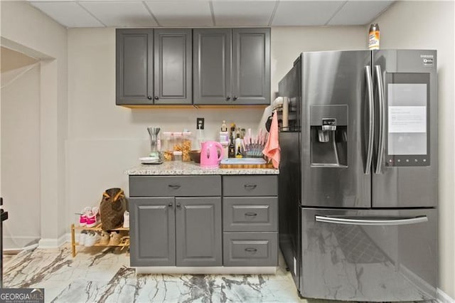 kitchen with light stone counters, a paneled ceiling, gray cabinets, and stainless steel fridge with ice dispenser