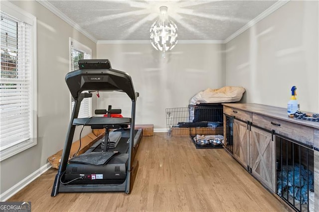 exercise area featuring ornamental molding, light hardwood / wood-style floors, a textured ceiling, and a notable chandelier