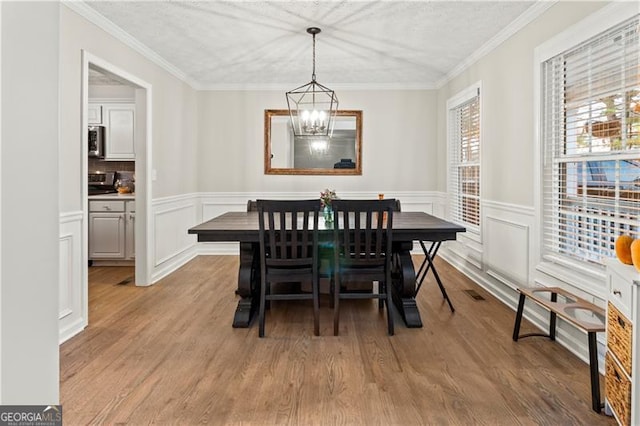 dining area with ornamental molding, a notable chandelier, and light hardwood / wood-style flooring