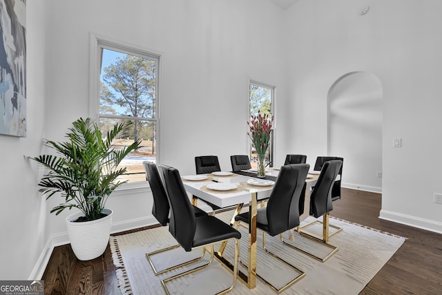 dining area featuring a towering ceiling, dark hardwood / wood-style flooring, and a wealth of natural light