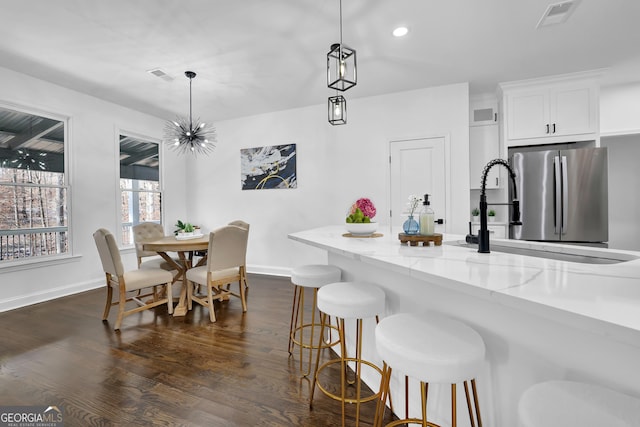 kitchen with light stone countertops, white cabinets, stainless steel refrigerator, and decorative light fixtures