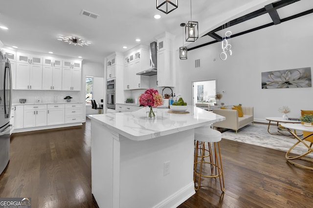 kitchen with wall chimney range hood, white cabinetry, light stone countertops, decorative backsplash, and decorative light fixtures