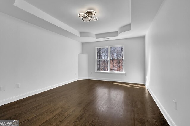 empty room with dark hardwood / wood-style flooring and a raised ceiling