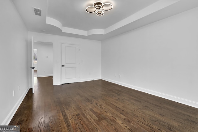 spare room featuring a raised ceiling and dark wood-type flooring