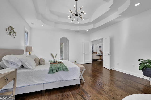 bedroom with dark hardwood / wood-style floors, a tray ceiling, and an inviting chandelier