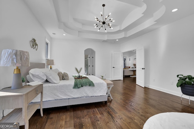 bedroom featuring a notable chandelier, a tray ceiling, dark wood-type flooring, and a high ceiling