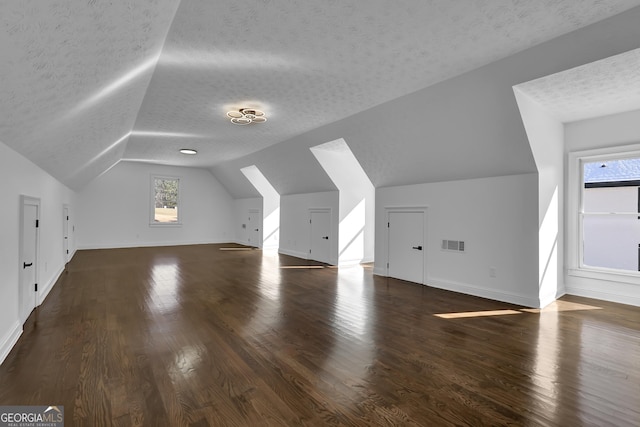 additional living space with dark wood-type flooring, vaulted ceiling, and a textured ceiling