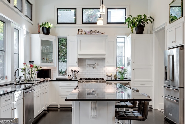 kitchen with appliances with stainless steel finishes, a breakfast bar, sink, hanging light fixtures, and custom range hood