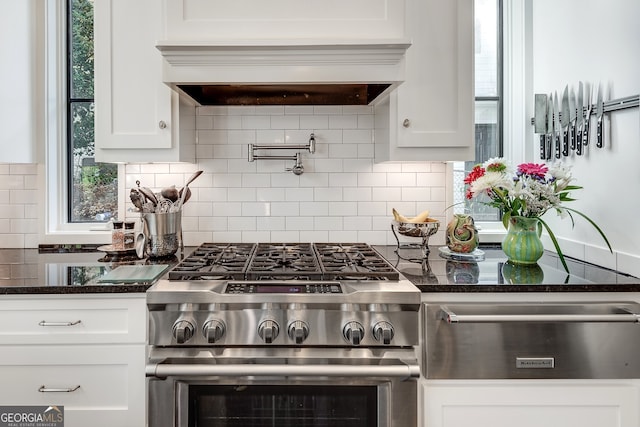 kitchen featuring white cabinetry, backsplash, dark stone counters, custom exhaust hood, and stainless steel range with gas stovetop