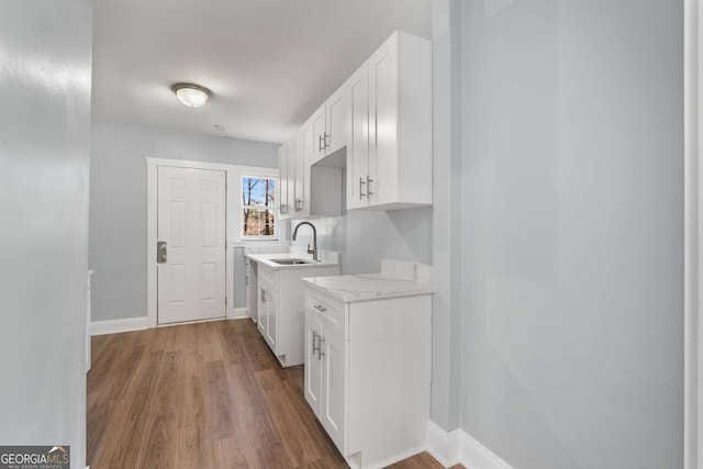 kitchen with light stone countertops, sink, hardwood / wood-style floors, and white cabinets