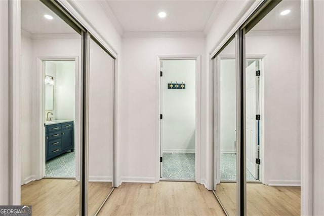 hall with light wood-type flooring, ornamental molding, and sink