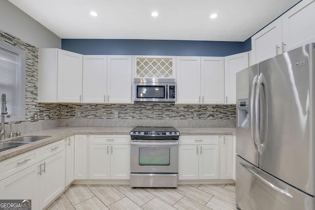 kitchen featuring sink, white cabinetry, appliances with stainless steel finishes, light stone countertops, and decorative backsplash