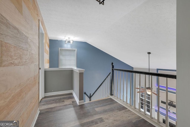 hall featuring vaulted ceiling, hardwood / wood-style floors, and a textured ceiling