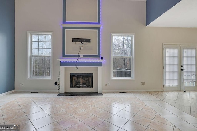 unfurnished living room featuring plenty of natural light, a towering ceiling, light tile patterned floors, and french doors