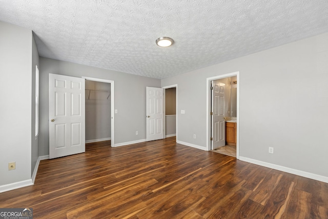 unfurnished bedroom featuring connected bathroom, dark hardwood / wood-style flooring, a closet, and a spacious closet