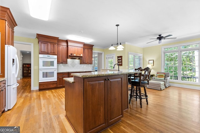 kitchen with white appliances, light wood-style floors, crown molding, a kitchen breakfast bar, and tasteful backsplash