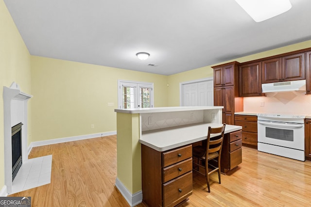 kitchen featuring a tile fireplace, light countertops, electric stove, under cabinet range hood, and a kitchen breakfast bar