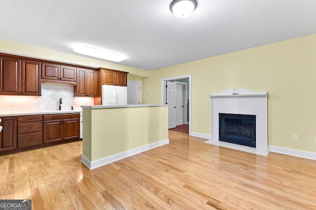 kitchen with a sink, backsplash, light wood-style floors, white fridge with ice dispenser, and light countertops