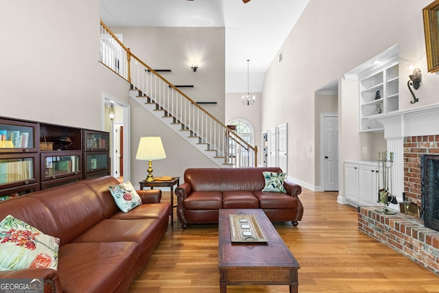 living area with stairway, baseboards, light wood-style flooring, a fireplace, and a towering ceiling