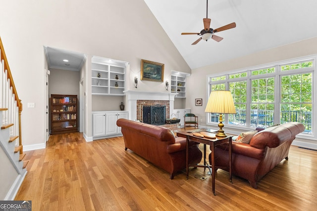 living room with stairway, baseboards, high vaulted ceiling, light wood-style flooring, and a brick fireplace