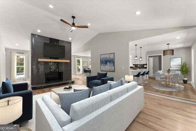 living room featuring lofted ceiling, a premium fireplace, ceiling fan, and light wood-type flooring