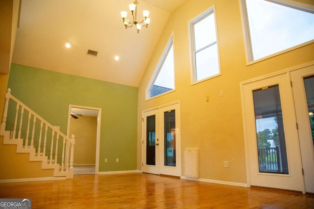 unfurnished living room featuring high vaulted ceiling, a chandelier, wood-type flooring, and french doors