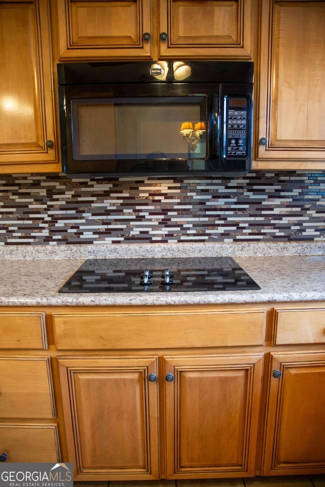 kitchen featuring black appliances, backsplash, and light stone counters