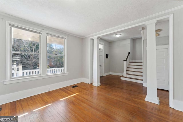 interior space with wood-type flooring, decorative columns, a textured ceiling, and crown molding