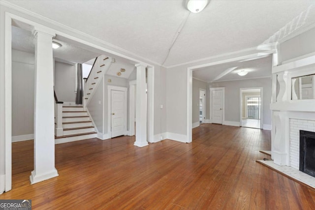 unfurnished living room featuring crown molding, vaulted ceiling, ornate columns, and a fireplace