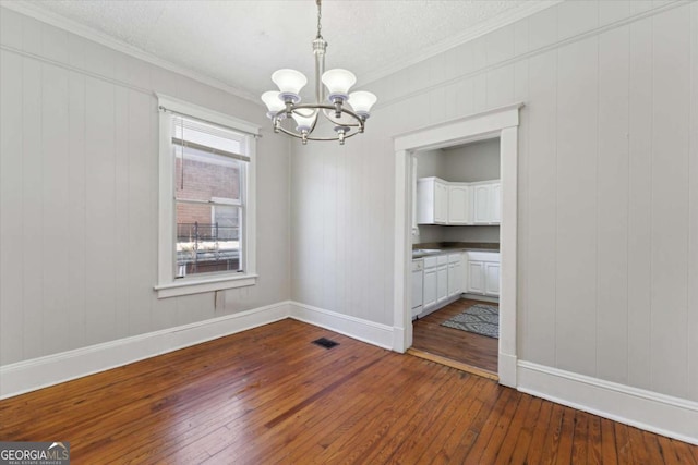 unfurnished dining area with dark wood-type flooring, a textured ceiling, crown molding, and a chandelier