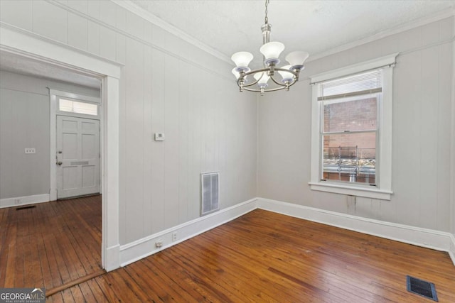 unfurnished dining area with crown molding, hardwood / wood-style floors, and an inviting chandelier