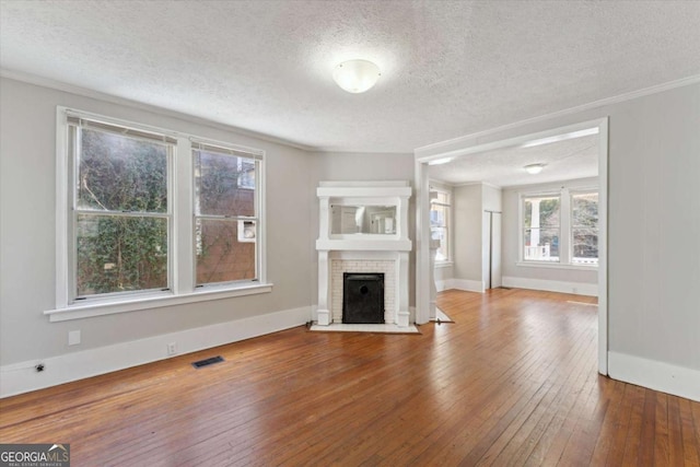 unfurnished living room with hardwood / wood-style flooring, a textured ceiling, ornamental molding, and a brick fireplace