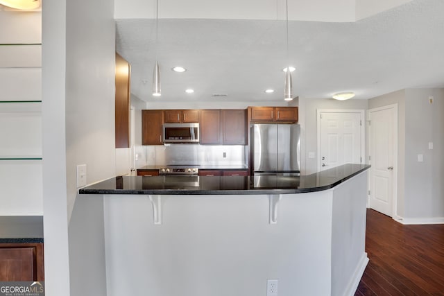 kitchen featuring kitchen peninsula, a kitchen bar, pendant lighting, and appliances with stainless steel finishes