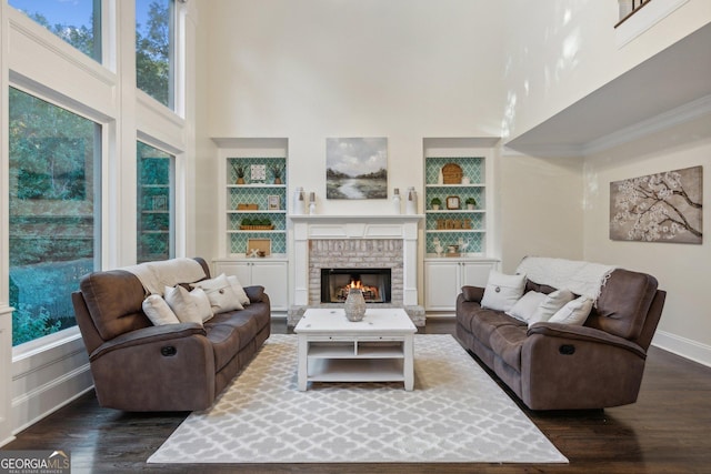 living room with built in shelves, dark hardwood / wood-style flooring, a towering ceiling, and a healthy amount of sunlight