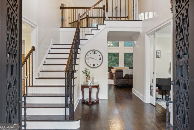 entryway featuring a towering ceiling, ornamental molding, and dark wood-type flooring