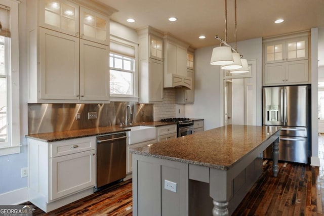 kitchen with a center island, appliances with stainless steel finishes, tasteful backsplash, pendant lighting, and dark stone counters