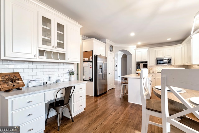 kitchen with a breakfast bar area, appliances with stainless steel finishes, tasteful backsplash, white cabinets, and dark hardwood / wood-style flooring