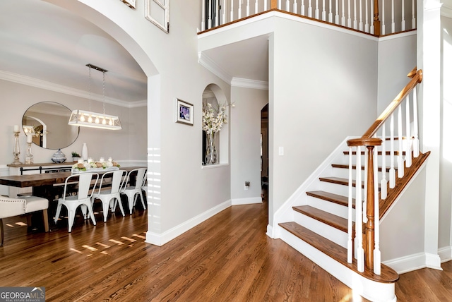 staircase featuring hardwood / wood-style flooring, ornamental molding, and a towering ceiling