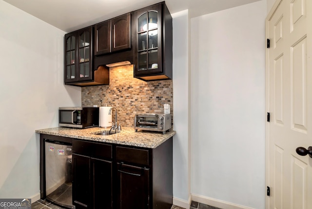 kitchen featuring appliances with stainless steel finishes, sink, backsplash, dark brown cabinetry, and light stone countertops