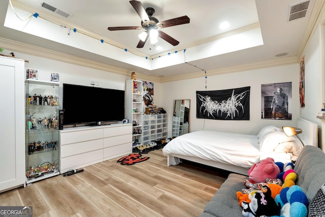 bedroom featuring crown molding, ceiling fan, a tray ceiling, and light wood-type flooring