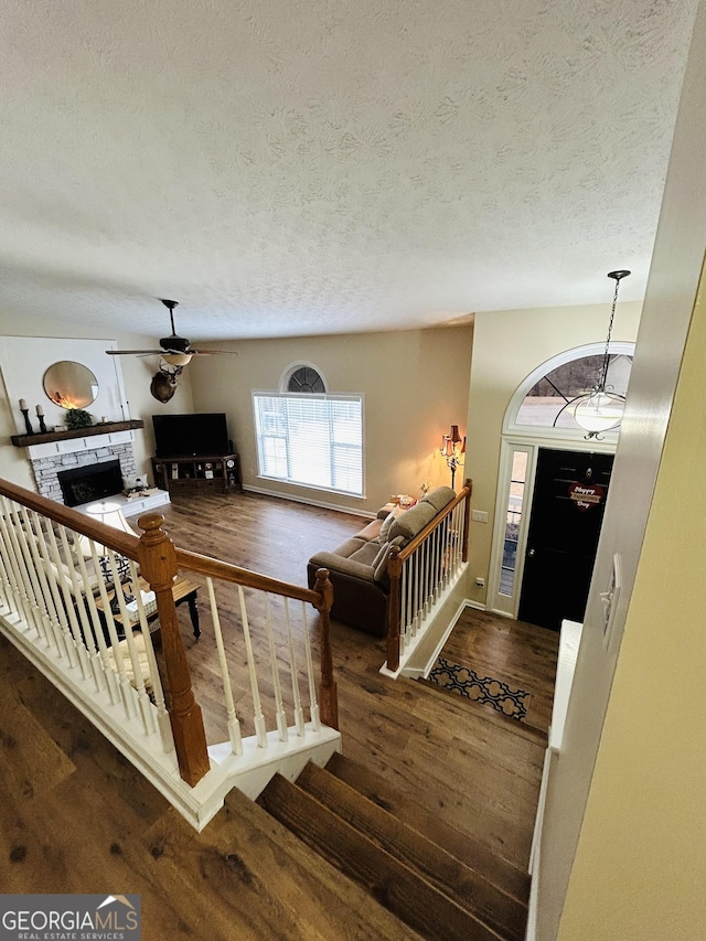 living room with ceiling fan, a textured ceiling, a fireplace, and dark hardwood / wood-style flooring