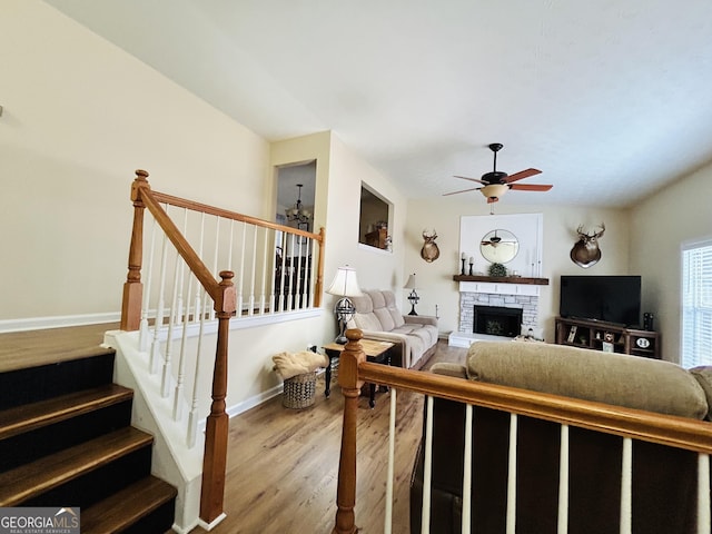 living room featuring wood-type flooring, ceiling fan, and a stone fireplace