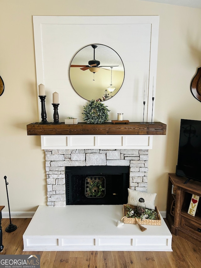 room details featuring ceiling fan, a stone fireplace, and wood-type flooring