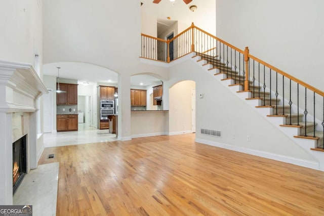 unfurnished living room with light wood-type flooring, ceiling fan, a towering ceiling, and a fireplace