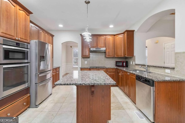 kitchen with a center island, stainless steel appliances, decorative backsplash, sink, and stone countertops