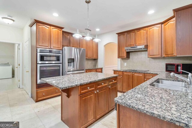 kitchen with appliances with stainless steel finishes, a kitchen island, decorative light fixtures, decorative backsplash, and sink