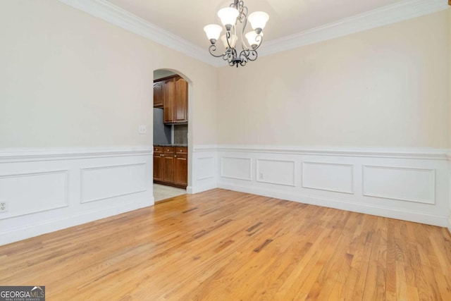 spare room with a chandelier, ornamental molding, and light hardwood / wood-style floors