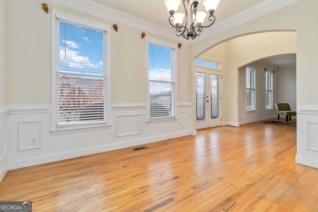 unfurnished room featuring light wood-type flooring, ornamental molding, and an inviting chandelier