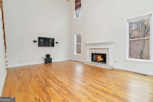 unfurnished living room with a towering ceiling, a high end fireplace, and light hardwood / wood-style floors