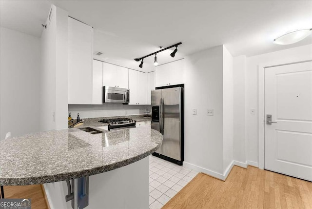 kitchen with kitchen peninsula, white cabinets, sink, and appliances with stainless steel finishes